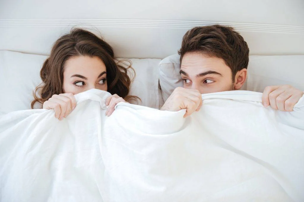 Funny young couple lying and hiding under the blanket in bed